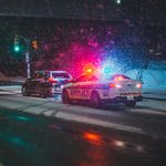 Police car with flashing lights during a snowy night on a city road.