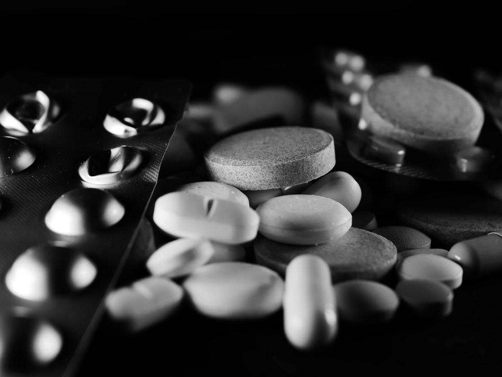 Black and white close-up of various pills and capsules, showcasing pharmaceutical diversity.
